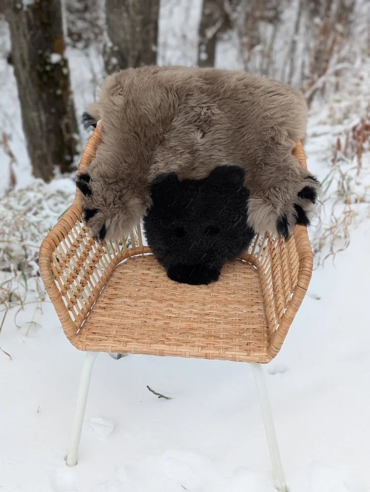 Hand made furry brown and black grizzly bear rug made of soft merino sheepskin resting on a wicker chair