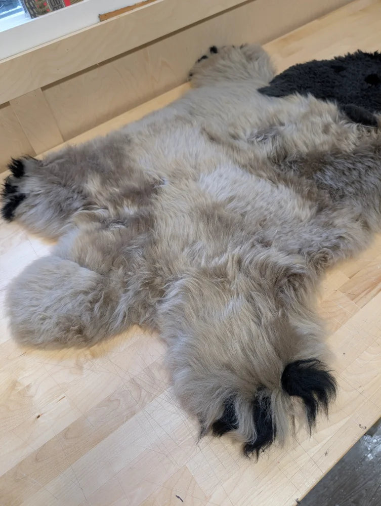 A hand made gray and black merino sheepskin grizzly bear rug shaped like a plush faux fur lying on a wooden floor