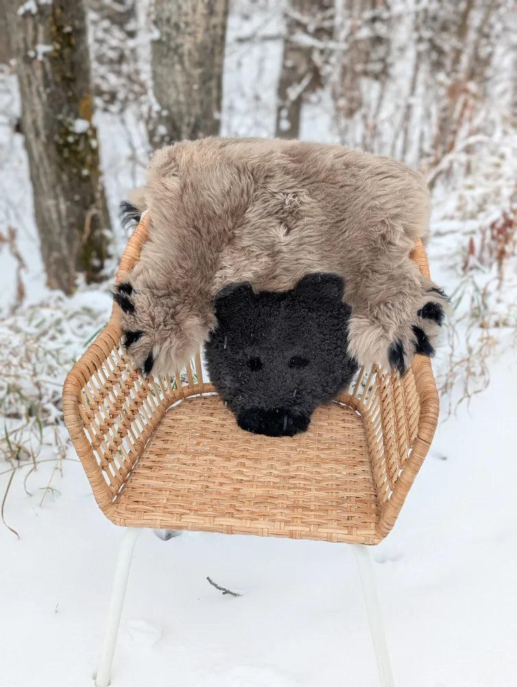 Furry beige and black bear shaped merino sheepskin rug resting on a wicker chair handmade grizzly bear rug