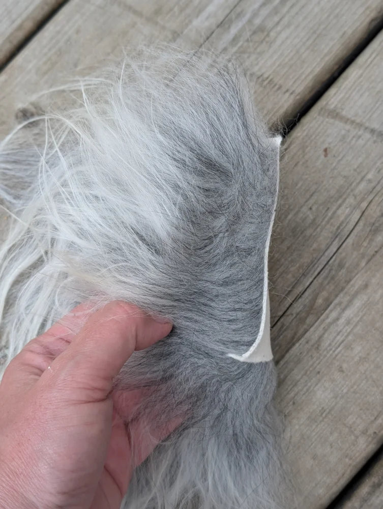 Fluffy gray and white sheepskin sample square with stitched edge showing soft faux fur texture
