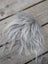 A fluffy silver-gray sheepskin sample square with long wavy faux fur strands lying on a wooden surface