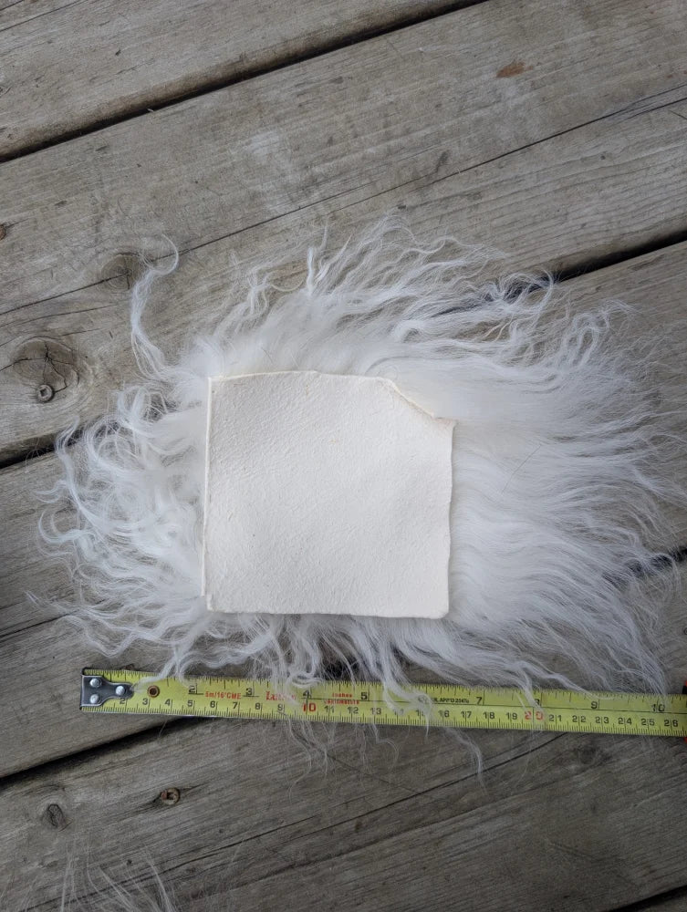 White fluffy sheepskin sample square with a square cutout showing soft wool texture and natural leather backing