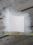 White rectangular sheepskin sample square with fluffy fur edges resting on wood with measuring tape below