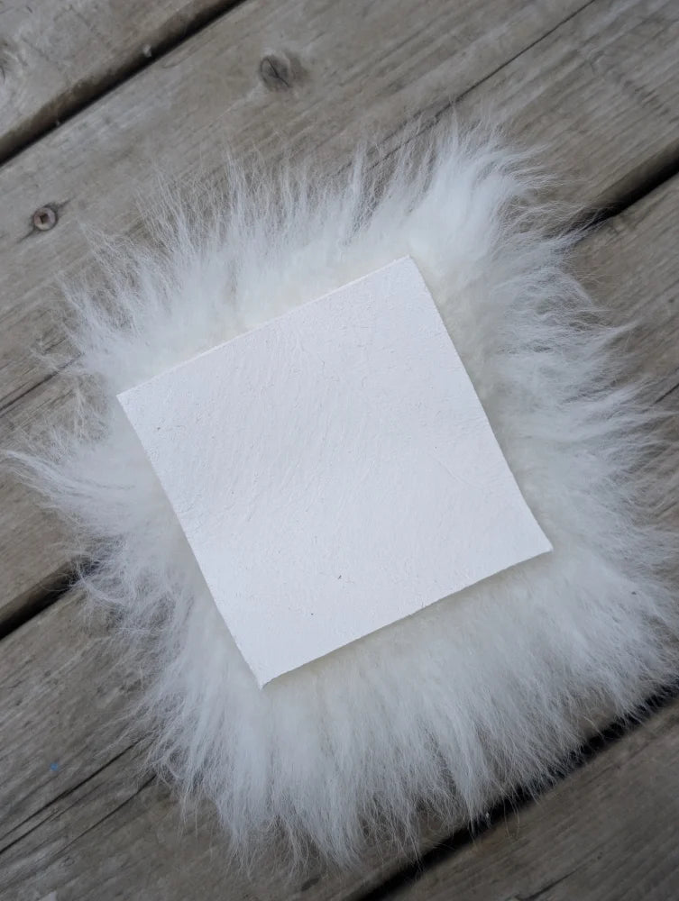 White square felt pad surrounded by fluffy white faux fur sheepskin sample squares for soft fabric feel