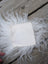 A square off-white textured sheepskin sample fabric rests on fluffy white wool fibers for touch and feel testing