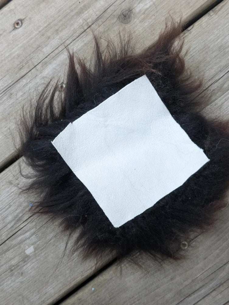 A white leather sheepskin sample square with a fluffy black faux fur border for fabric testing and design