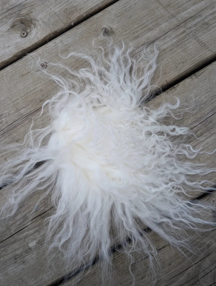 A fluffy white curly sheepskin sample square resting on a wooden surface for texture and quality testing