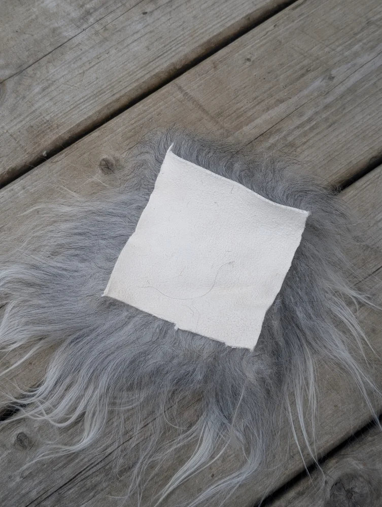 A white leather sheepskin sample square resting on soft gray fur showing texture and material quality