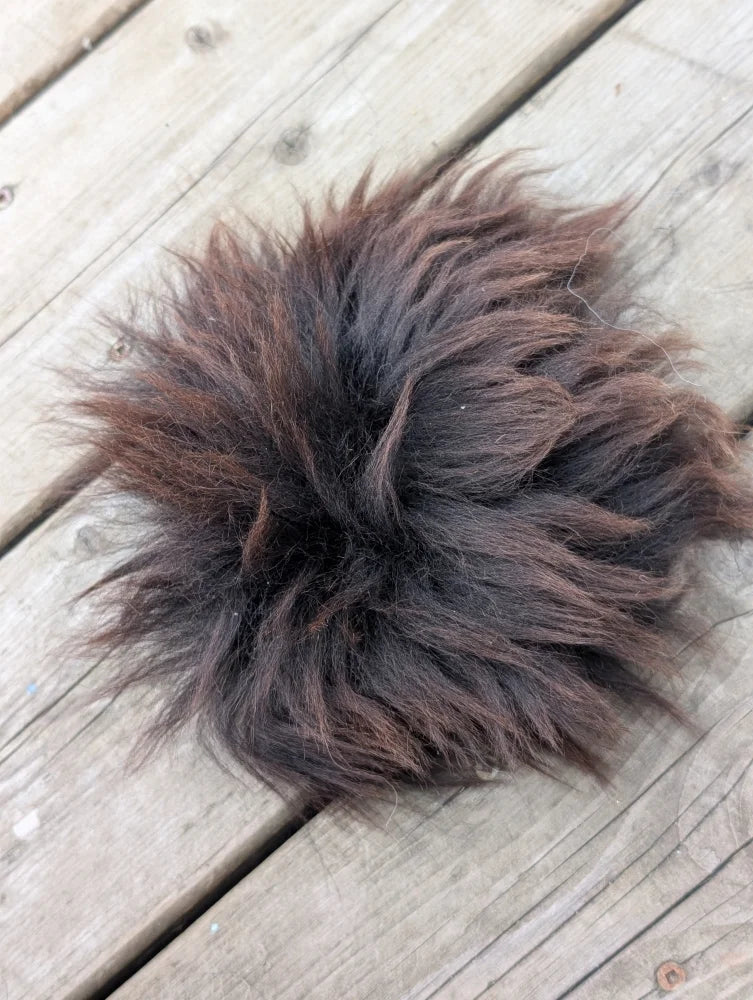A fluffy dark brown faux fur pom pom with soft texture shown on sheepskin sample squares