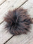 A fluffy dark brown faux fur pom pom with soft texture shown on sheepskin sample squares