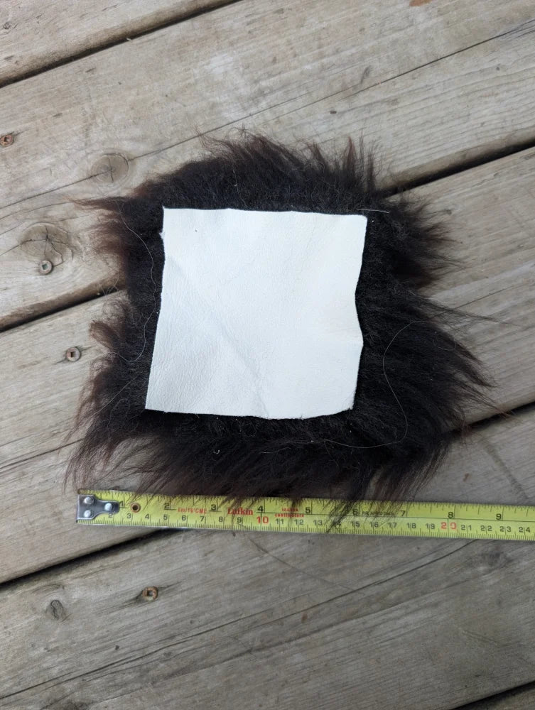 A square white sheepskin sample napkin surrounded by dark brown fluffy sheepskin fur for texture testing