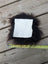 A square white sheepskin sample napkin surrounded by dark brown fluffy sheepskin fur for texture testing