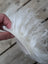 A hand holds a white fluffy curly sheepskin sample square made of soft wool fiber material