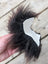 A hand holds a dark brown fluffy faux fur sheepskin sample square with a white paper cutout attached