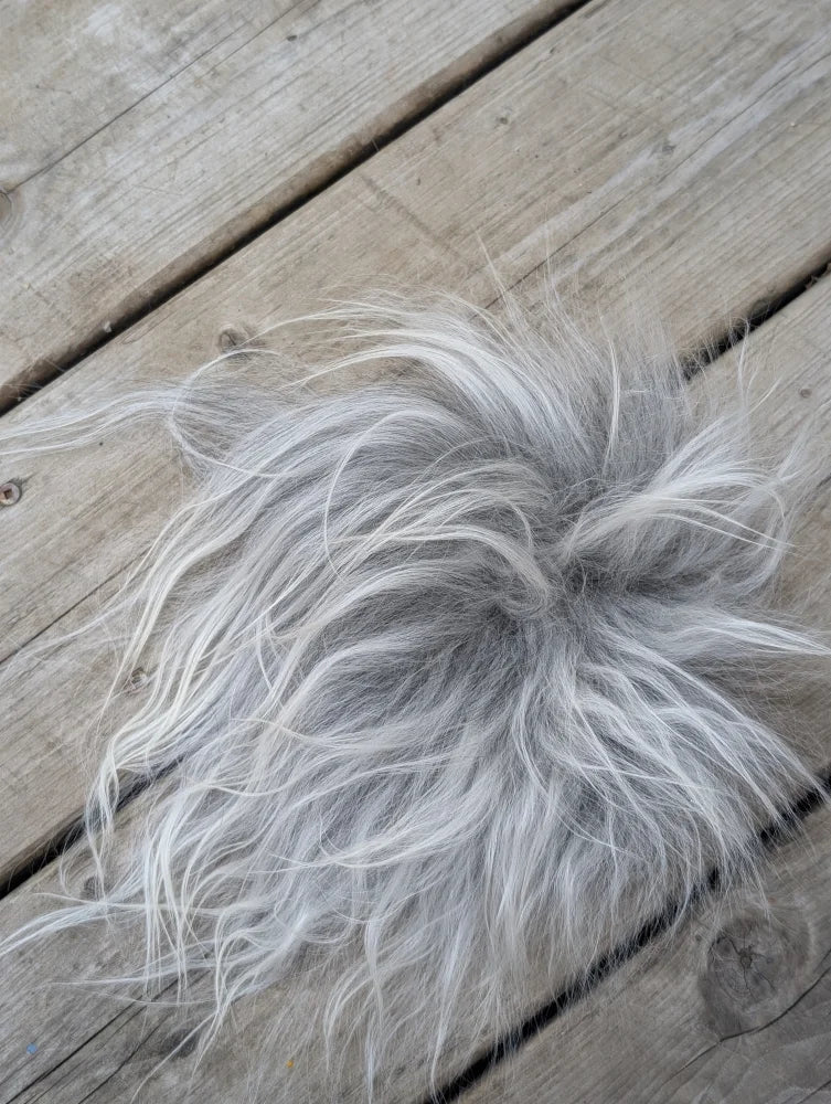 A fluffy silver-gray faux fur pom-pom on a wooden surface as part of sheepskin sample squares