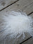 A fluffy white curly sheepskin fiber sample square resting on a wooden surface for soft texture testing