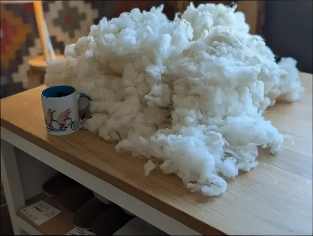 Fluffy cotton ball on wooden table with mug, like Canadian sheep’s wool sheepskin pet bed