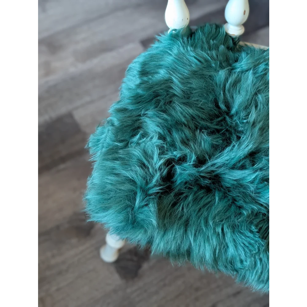 Teal faux fur purse with white wooden handles on gorgeous green merino sheepskin chair pads
