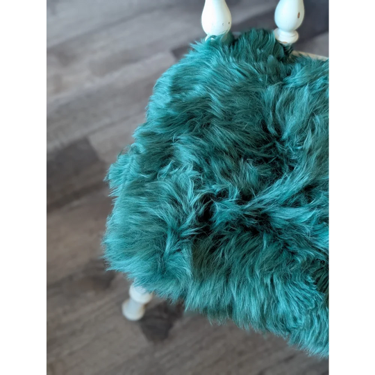 Teal faux fur purse with white wooden handles on gorgeous green merino sheepskin chair pads