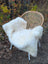 A plush white british isles sheepskin rug draped over a woven wicker chair with metal legs for soft comfort