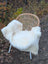 A cozy white british isles sheepskin throw draped over a wicker chair with slim metal legs