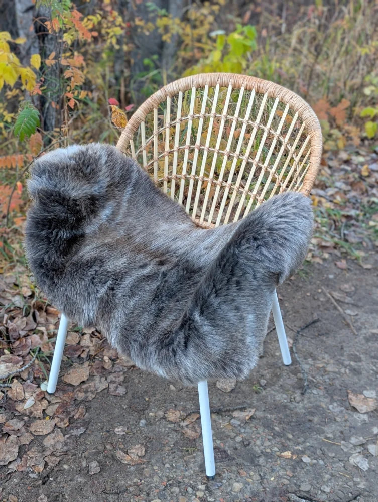 Gray faux fur british isles sheepskin chair cover draped over woven wicker chair with white metal legs