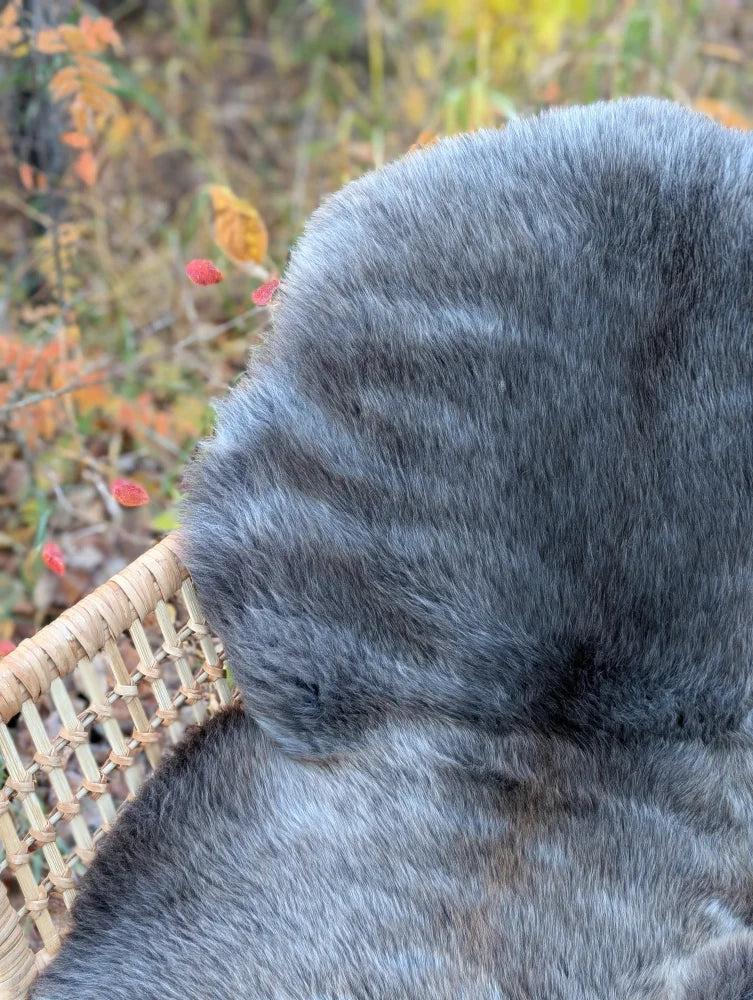 A softbrit#2 gray faux fur throw draped over a wicker basket showcasing british isles sheepskin style