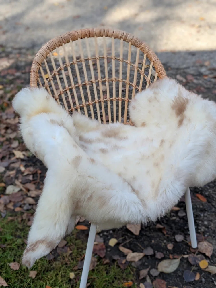 A soft brit 4 british isles sheepskin throw in white and beige faux fur draped over a woven wicker chair
