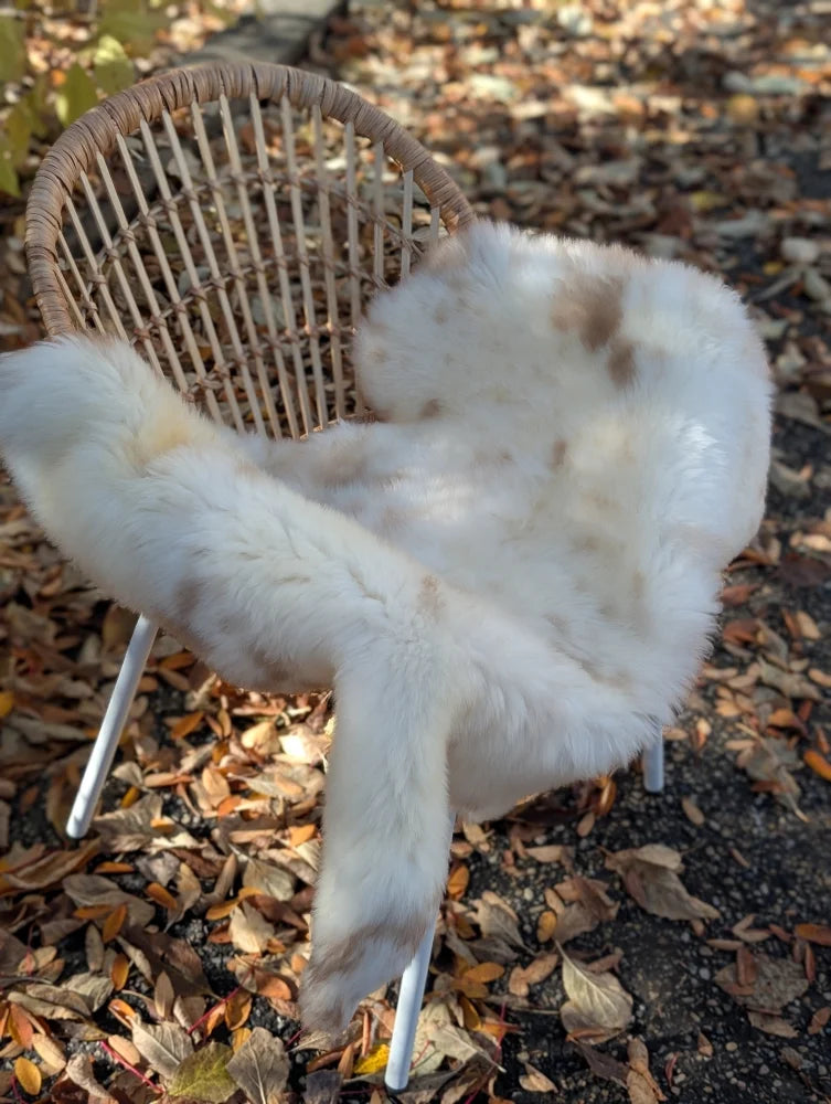A plush white and light brown faux isles sheepskin throw draped over a woven wicker chair for cozy use