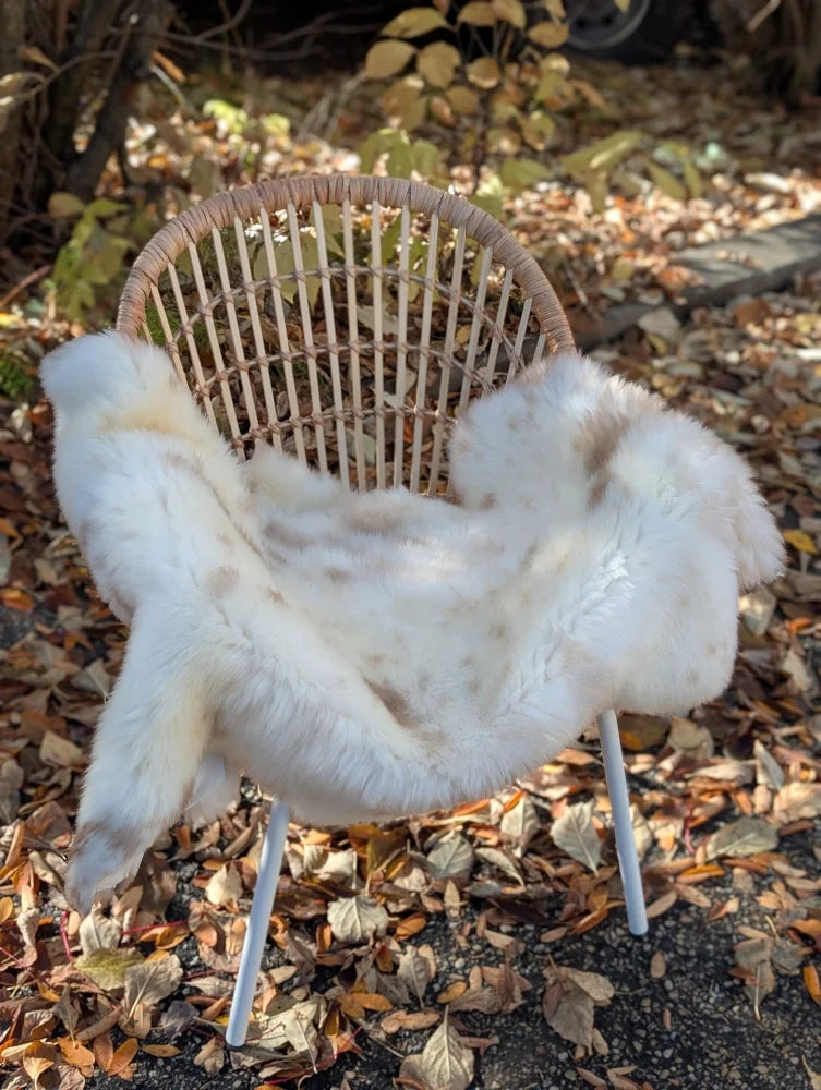 White faux fur throw blanket with subtle brown speckles draped on wicker chair soft british isles sheepskin