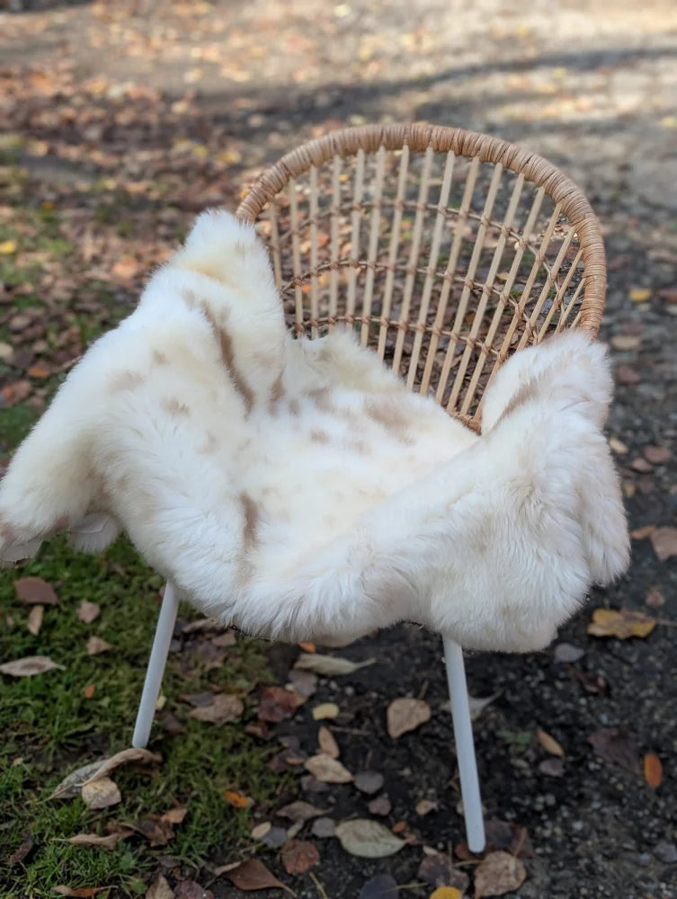 A cozy white faux fur throw with brown speckles draped over wicker chair soft british isles sheepskin