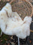 A cream british isles sheepskin rug with brown speckles resting on a woven wicker chair softbrit 47x28 inches
