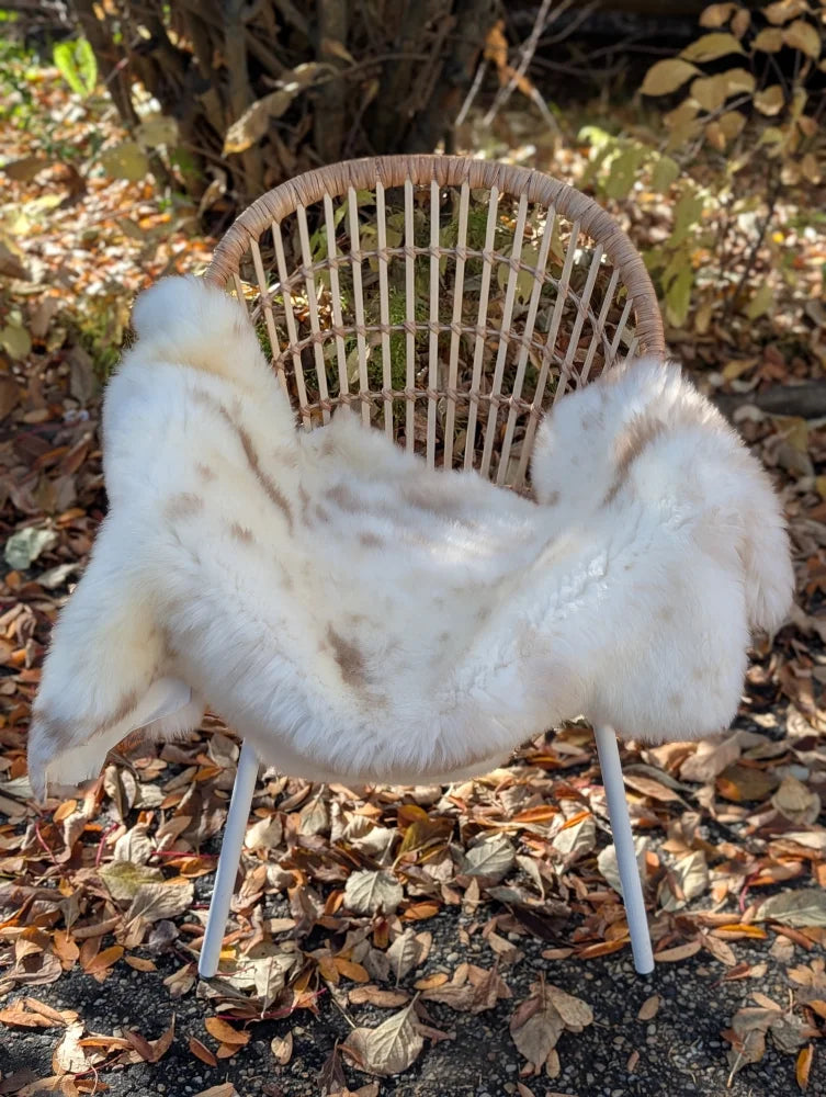 A softbrit#4 plush white faux fur throw with brown speckles draped on wicker chair made from british isles sheepskin