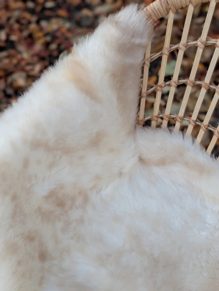 Fluffy cream-colored softbrit#5 very soft british isles sheepskin faux fur blanket draped over a woven wicker chair