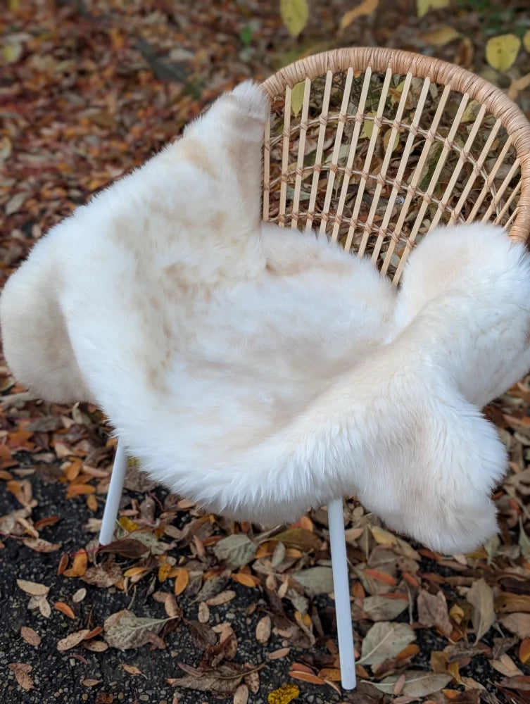 A softbrit#5 off-white faux fur throw draped on a rattan chair showcasing british isles sheepskin softness