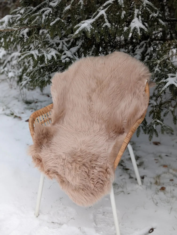 A light taupe merino sheepskin rug in peachy taupe draped over a wicker chair in snowy mid october outdoors