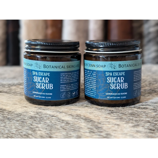 Two amber glass jars of spa escape sugar scrub by rae &amp; jenn soap with dead sea salt and essential oil blend