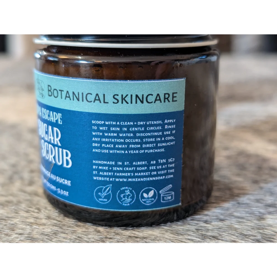 A dark brown glass jar with a blue label containing spa escape sugar scrub with dead sea salt and essential oil blend