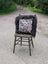 A cozy speckled cowhide cushion with white and brown spots sits on dark fur throw on olive green chair with long wool accents