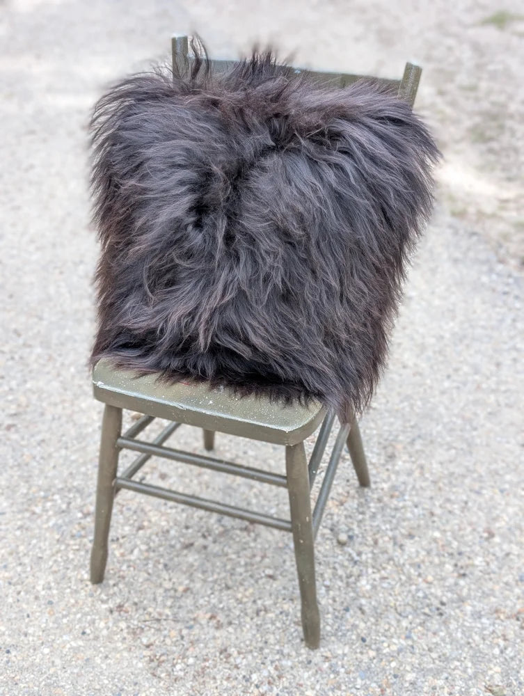 A plush dark gray speckled cowhide and browny black icelandic throw pillow with long wool fibers on a rustic chair