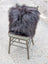 A plush dark gray speckled cowhide and browny black icelandic throw pillow with long wool fibers on a rustic chair