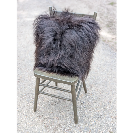A plush dark gray speckled cowhide and browny black icelandic throw pillow with long wool fibers on a rustic chair