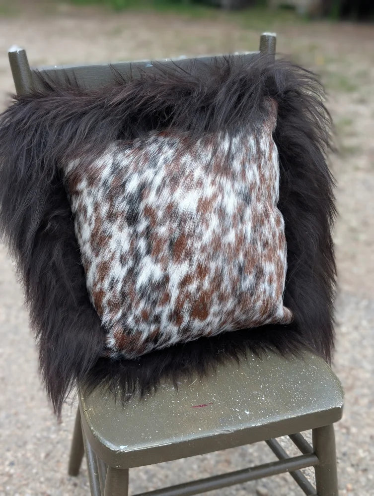 A square cushion featuring natural cowhide in browns white and black with thick long wool framing perfect for sewing machines use