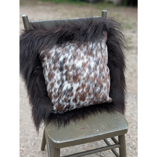 A square cushion featuring natural cowhide in browns white and black with thick long wool framing perfect for sewing machines use