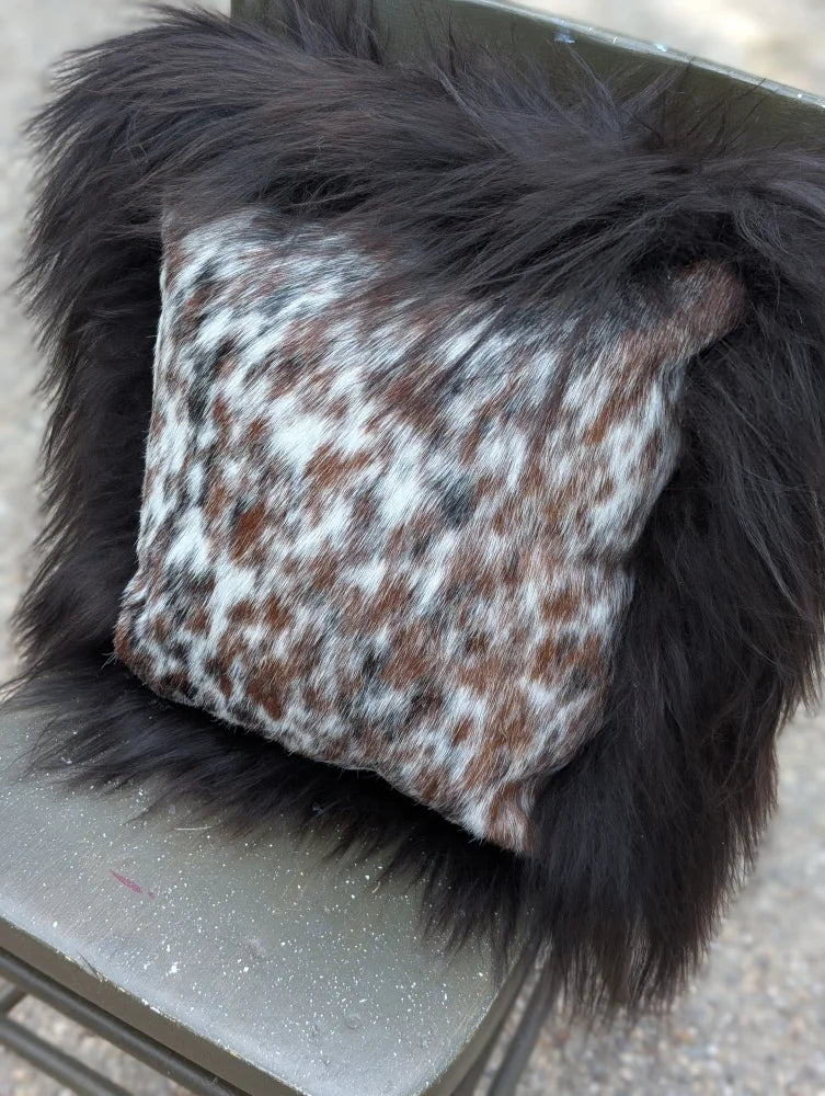 A cozy square pillow with natural cowhide speckled brown and white pattern framed by plush black long wool faux fur