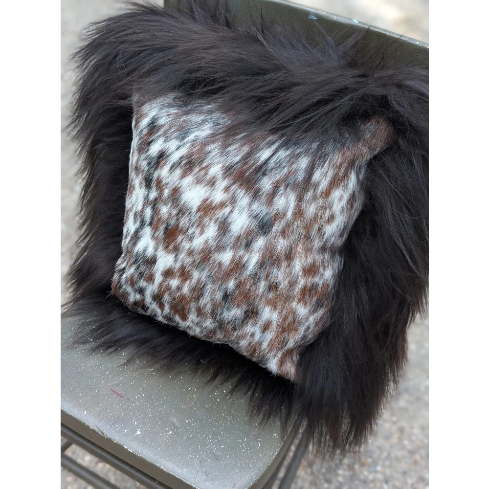 A cozy square pillow with natural cowhide speckled brown and white pattern framed by plush black long wool faux fur