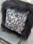 A cozy square pillow with natural cowhide speckled brown and white pattern framed by plush black long wool faux fur