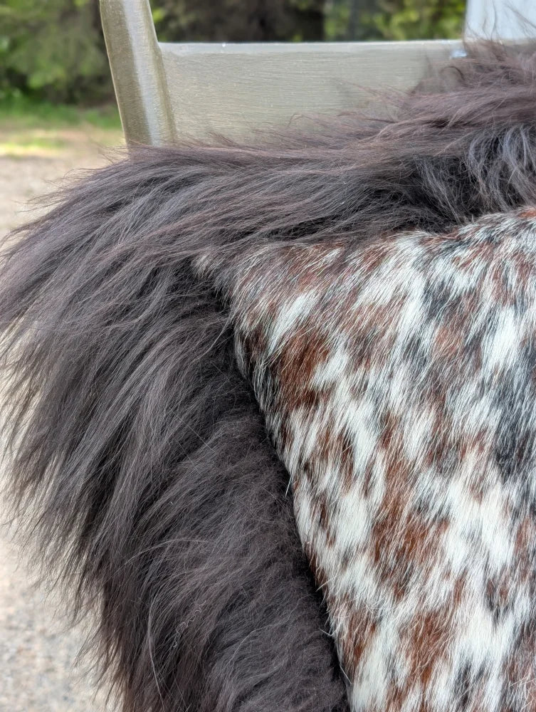 A plush speckled cowhide and browny black icelandic cushion with natural cowhide and soft long wool texture