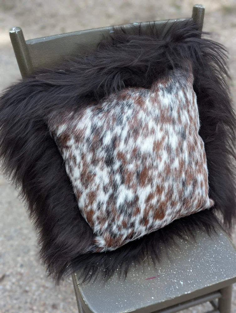 A cozy square pillow with natural cowhide speckled cowhide pattern framed by plush black long wool faux fur