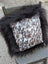 A cozy square pillow with natural cowhide speckled cowhide pattern framed by plush black long wool faux fur